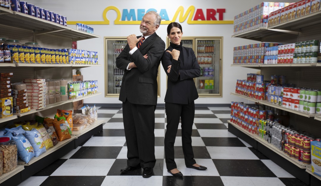 Dramcorp employees standing back to back pointing at each other inside Omega Mart