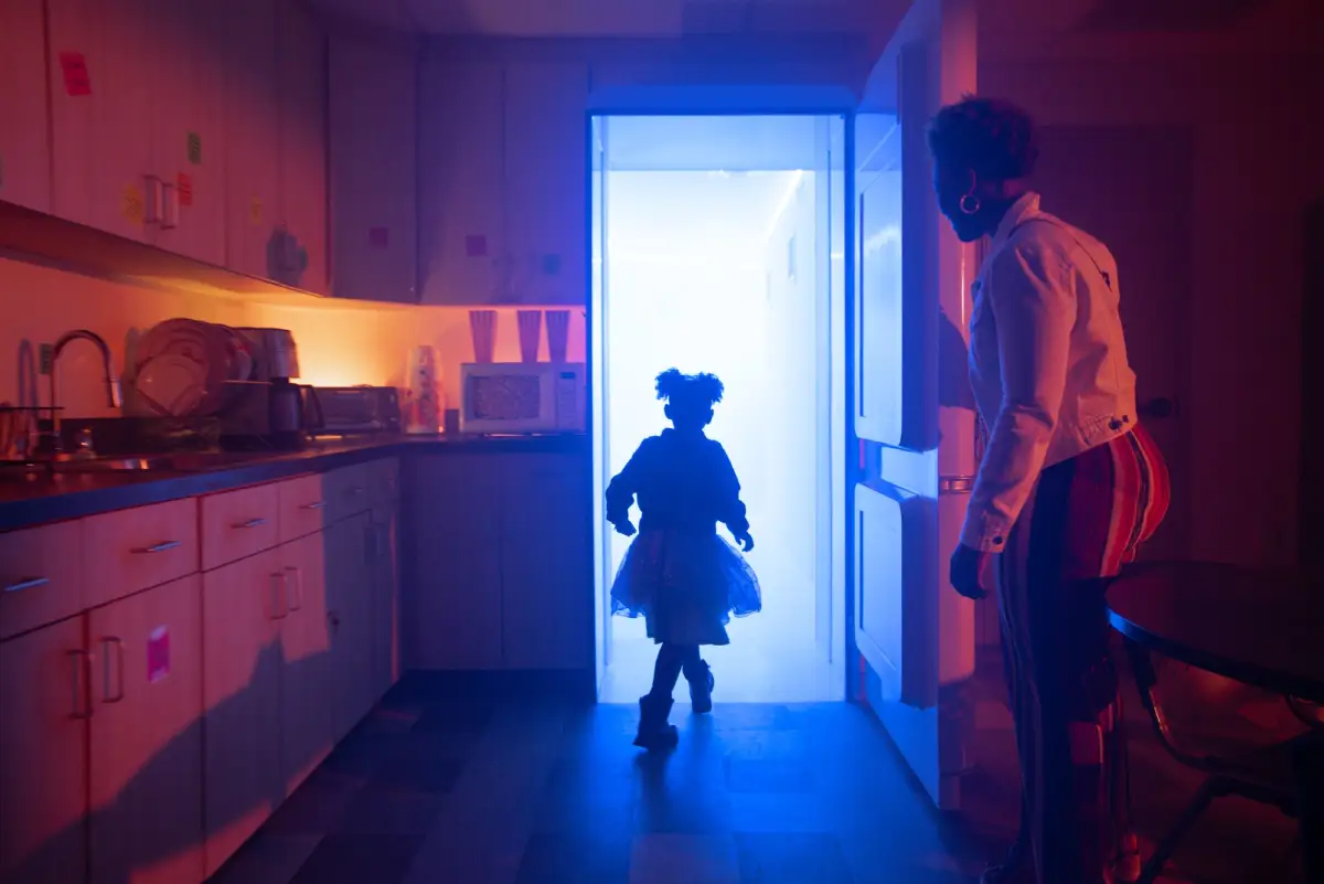 The silhouette of a child walking through a refrigerator doorway with a parent watching at Meow Wolf Houston.