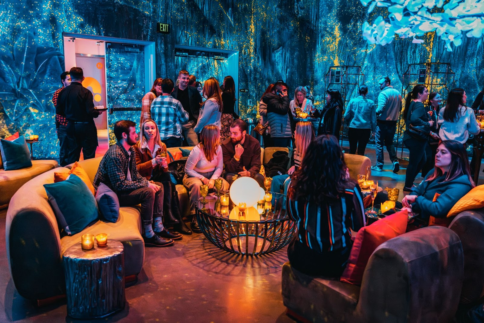 Guests socializing at Meow Wolf Denver's Perplexiplex event space with immersive art and glowing lounge decor.