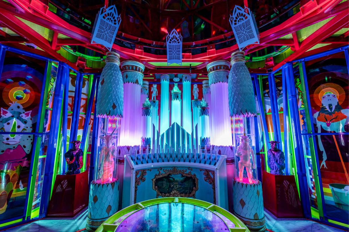 A set of organ pipes are lit up in blue and purple, stained glass on either side of the pipes.