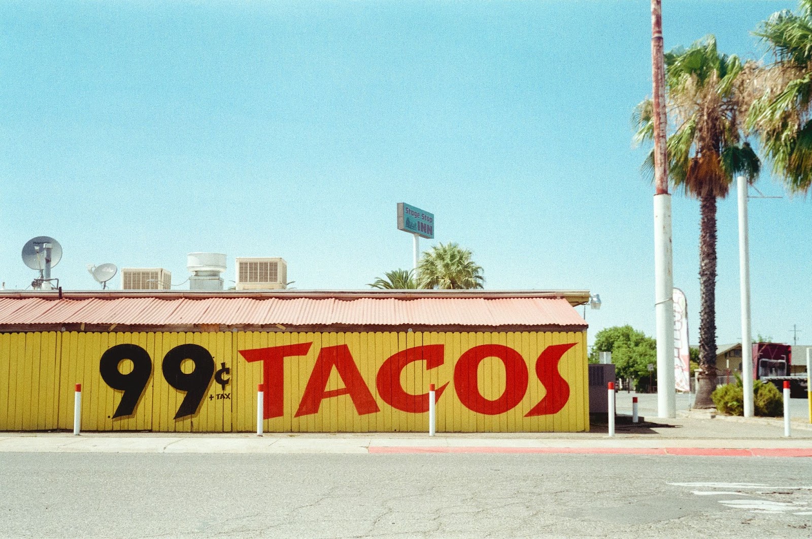 99c tacos on the side of a yellow building with a light blue sky and palm trees.