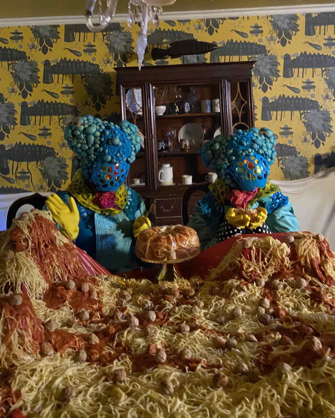 Two Meow Wolf creatures cradle spaghetti in their hands together amidst a mountain of spaghetti and meatballs.