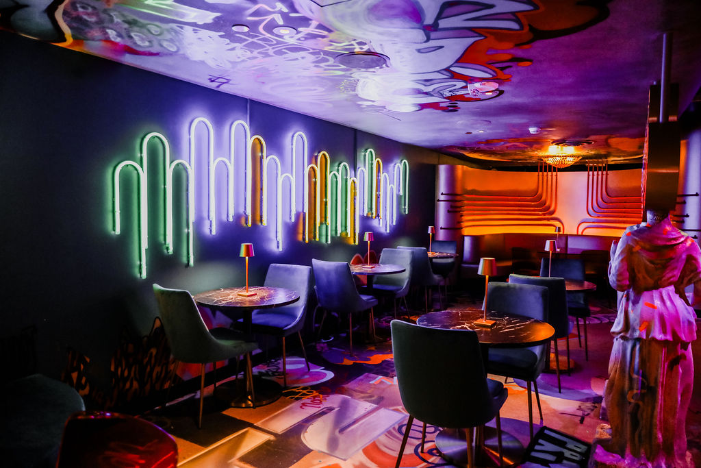 lounge bar space with art deco furniture with neon lights and grafitti all over inside Meow Wolf Denver