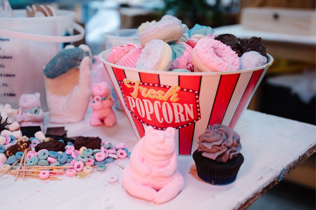 A popcorn bucket on a table with donuts in it and cereal bits around it.