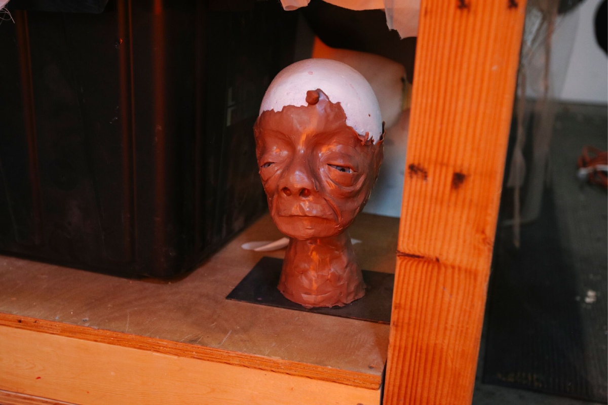 A clay shaping of a person's face on a wooden shelf.