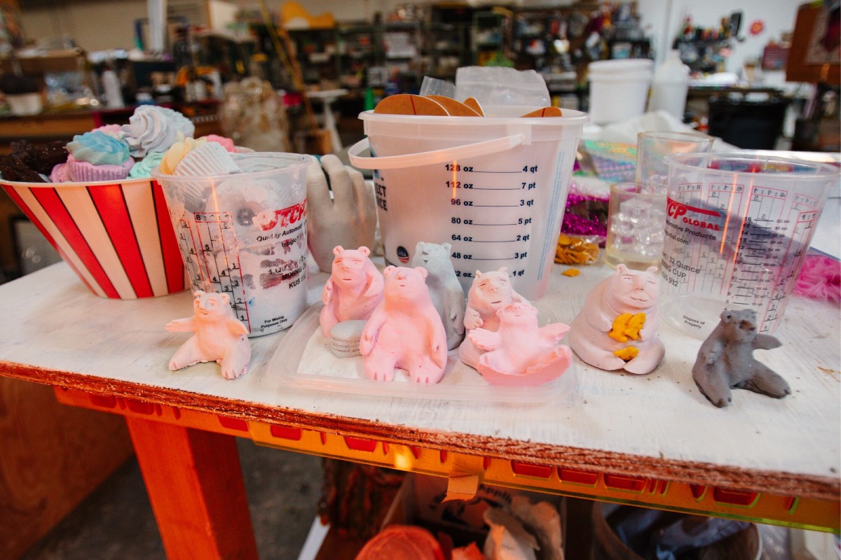 A set of pink and gray clay bears sit on a desk with buckets behind them.