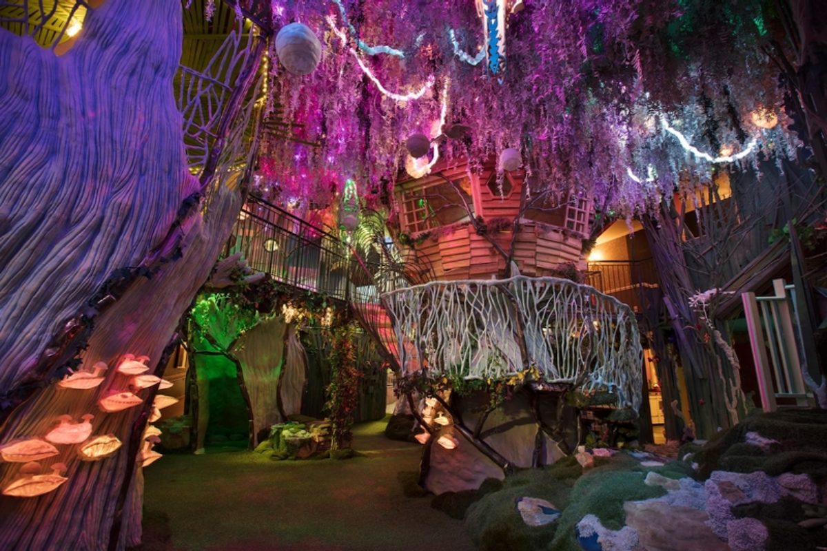 A wooden house sits in a otherworldly forest with lights throughout.