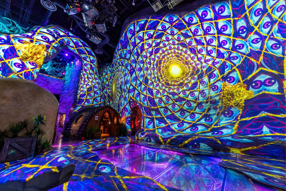 A room with projected screens and tessellating eyes and a dwelling in the back.