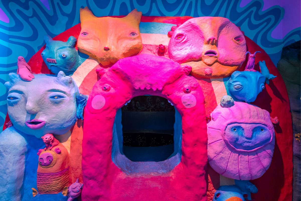 A collection of clay painted faces in orange, blue and pink with an opening in the mouth of the center being.