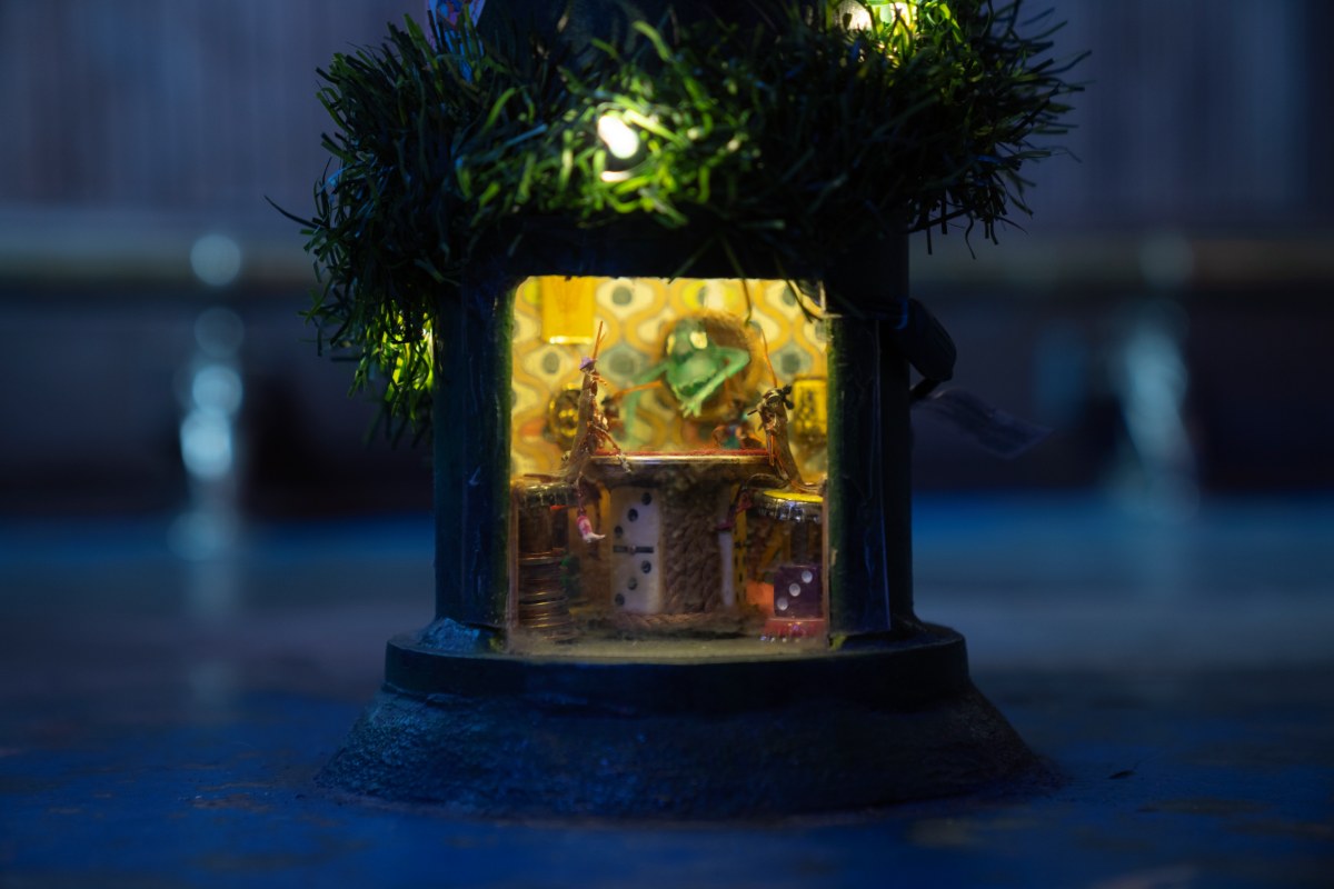 A small building with two roaches playing a game on a little table.