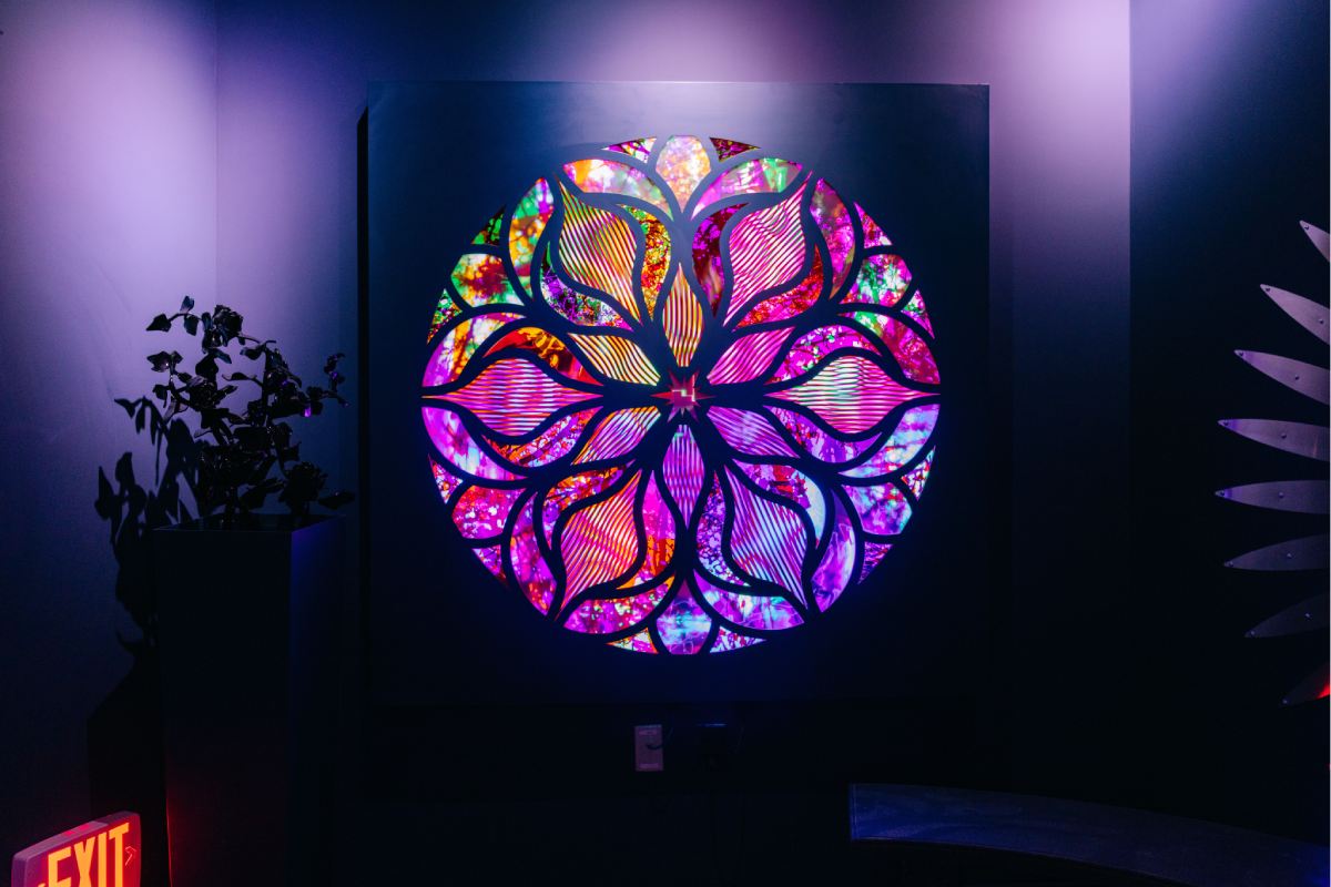 A colorful stained glass circle with intricate shapes in the center of a dark, dim-lit room.