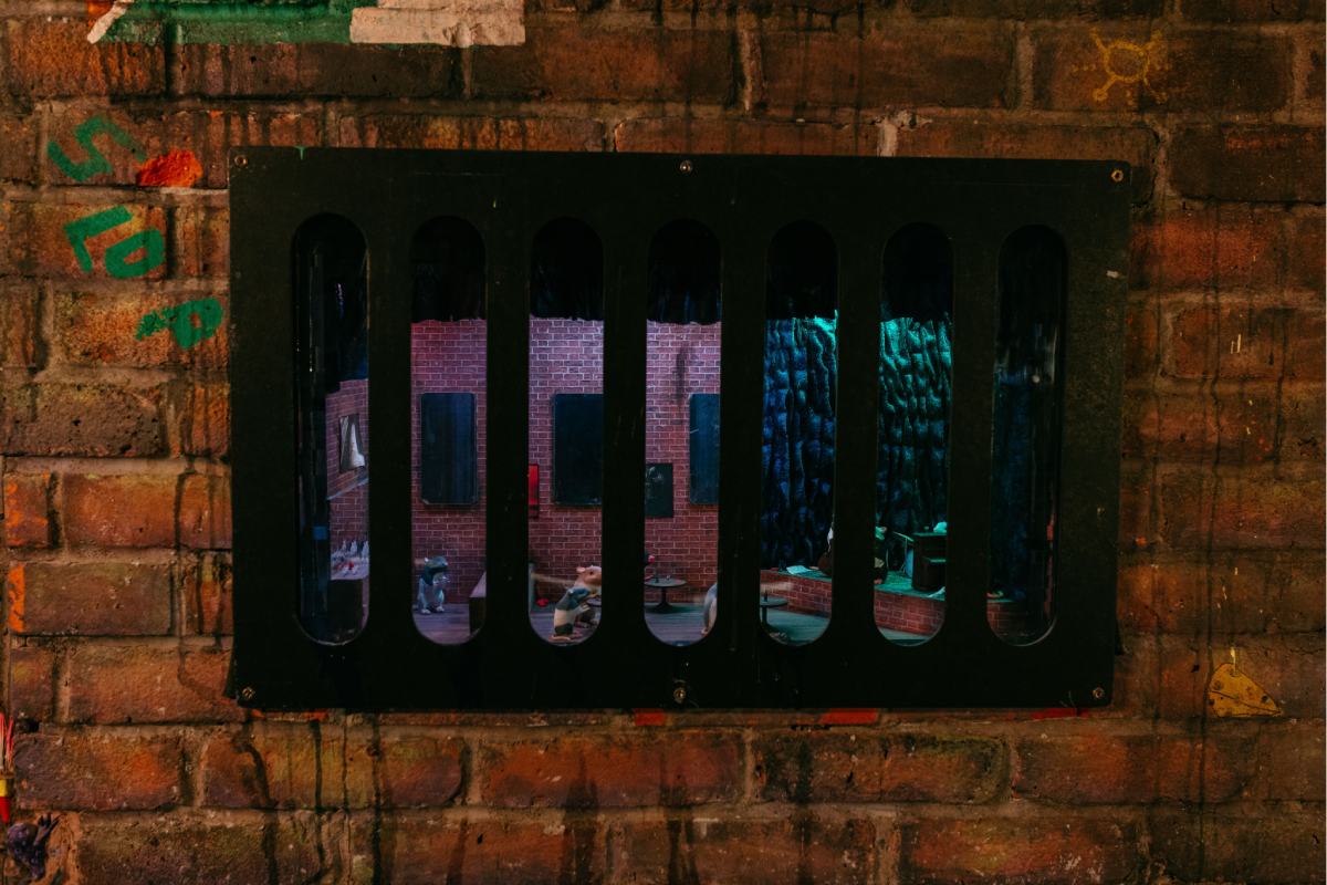 A brick wall with a black grate that has a diorama inside.i