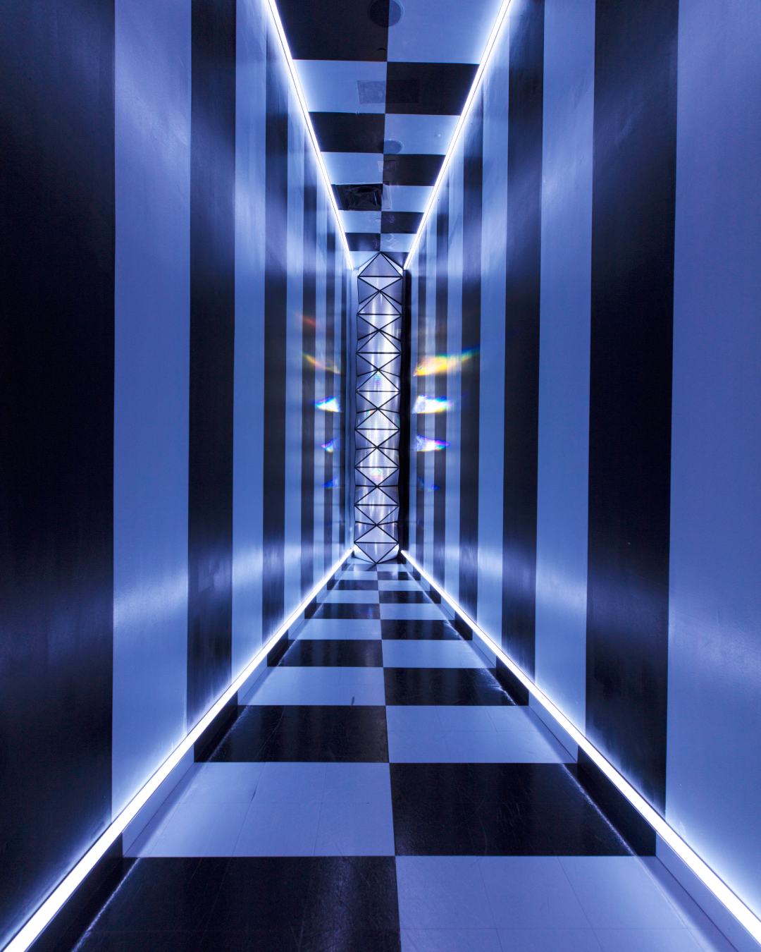 A black and white tiled and striped room with a light refracting crystal in the middle.