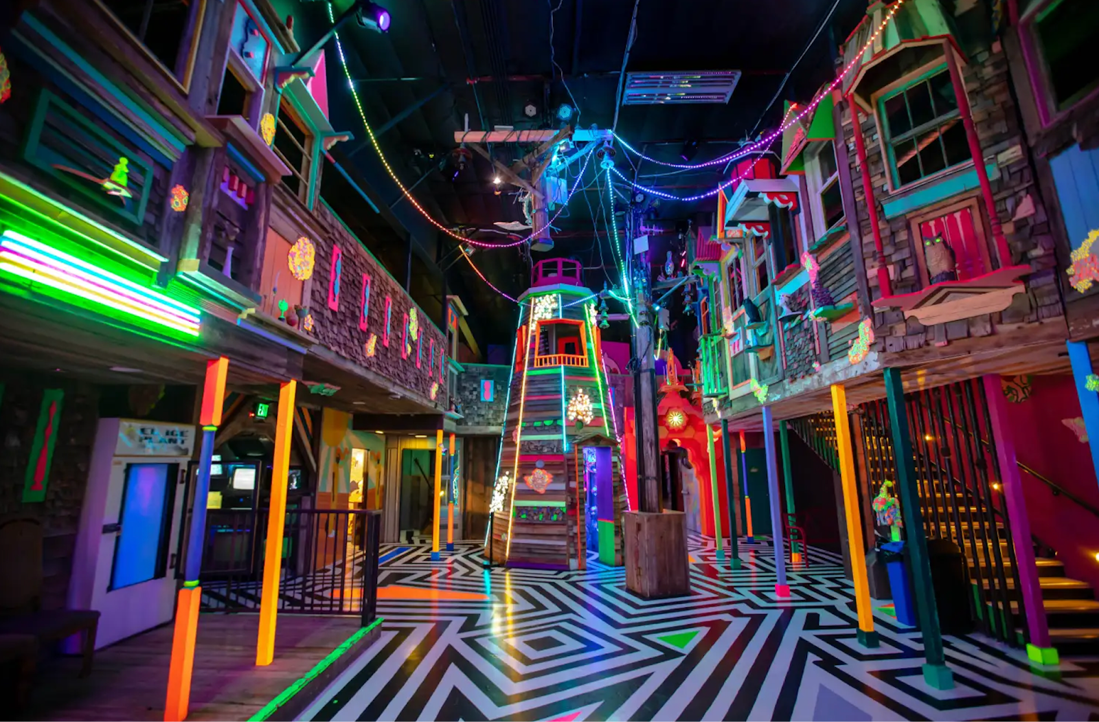 A room with various building fronts that have neon accents to them and a black and white patterned floor.