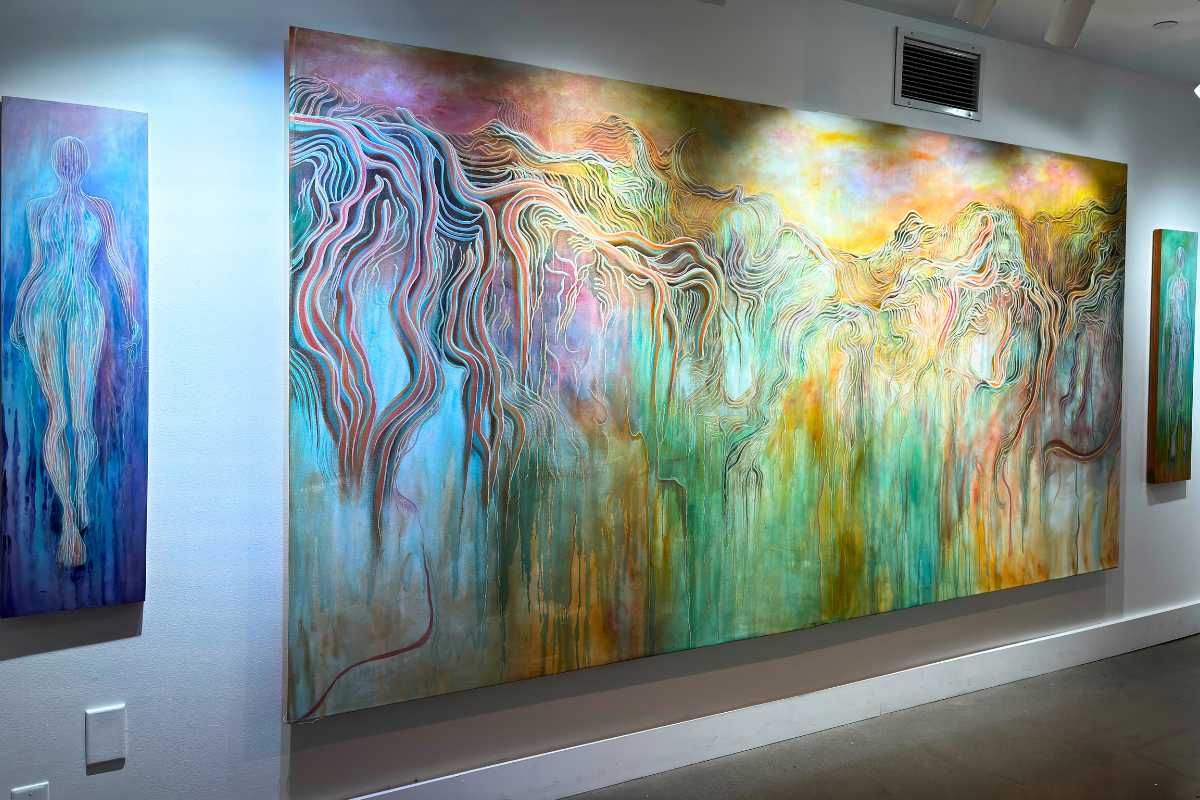 A painting of multiple pastel colors that look like they are dripping on the canvas, with two feminine paintings to either side.