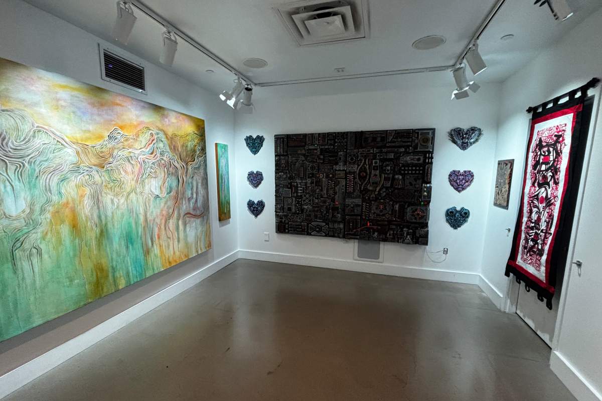 A gallery with 3 walls covered with a large colorful painting, a large electronic looking board, and a fabric door hanging.