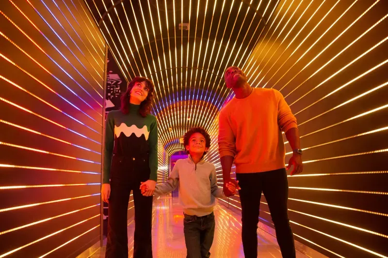 two parents and a child walking through a hallway with horizontal lights