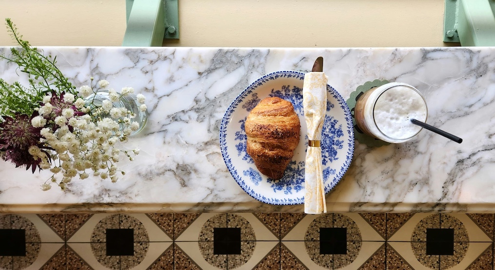 marble table with a croissant and coffee on ablue plate