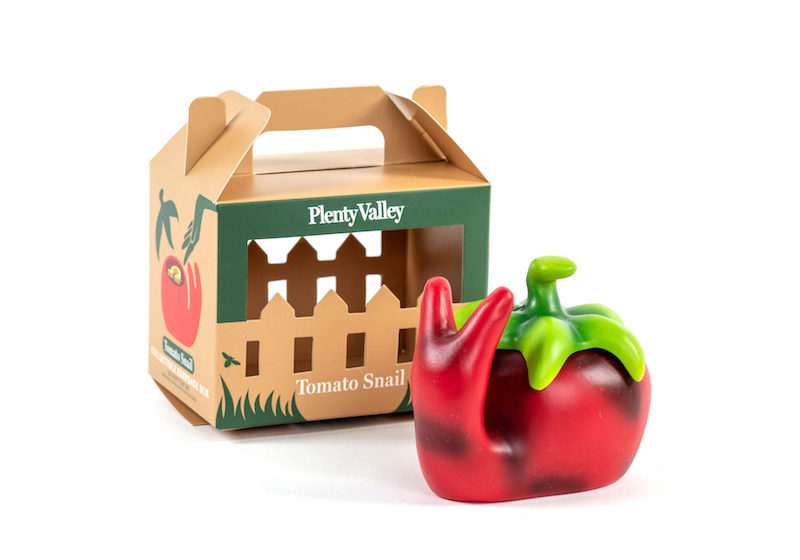 red plastic snail that looks similar to a tomato in front of a box with the words Plenty Valley.The box looks kind of like a fence with a handle on top.