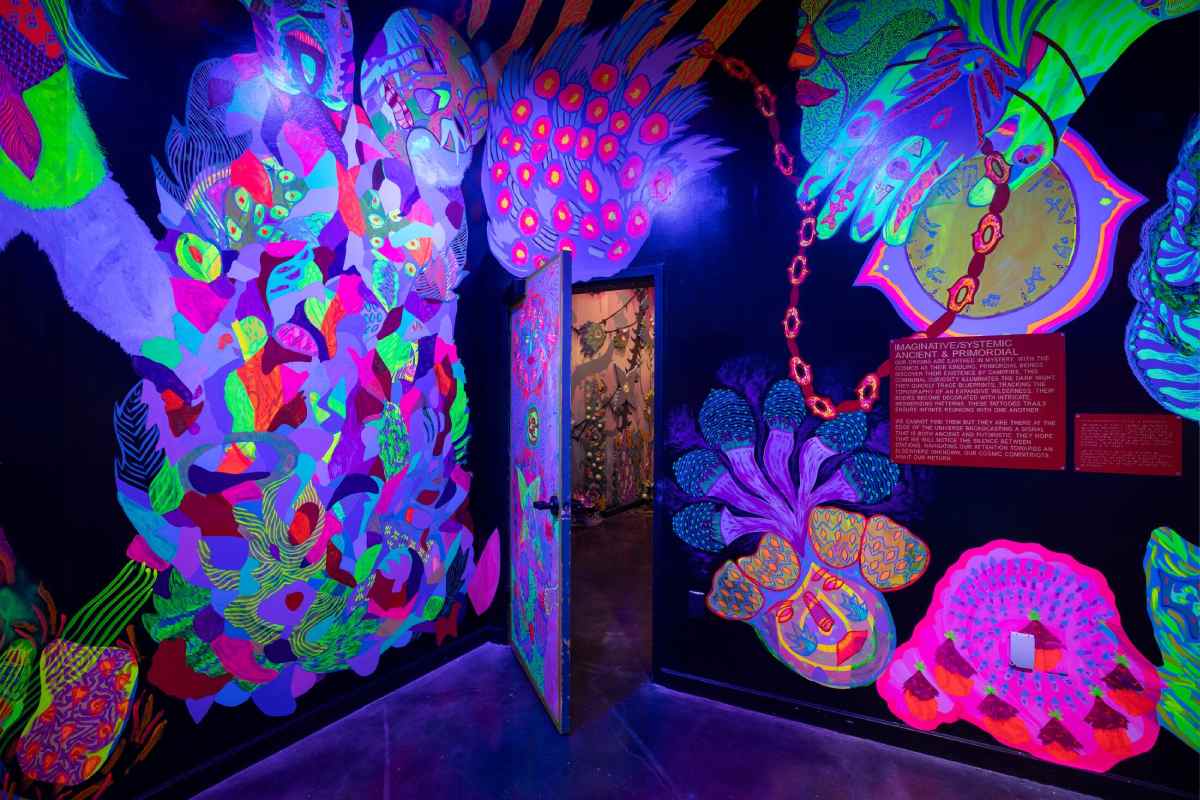 A dark room with neon paintings on the walls inside Meow Wolf Houston.
