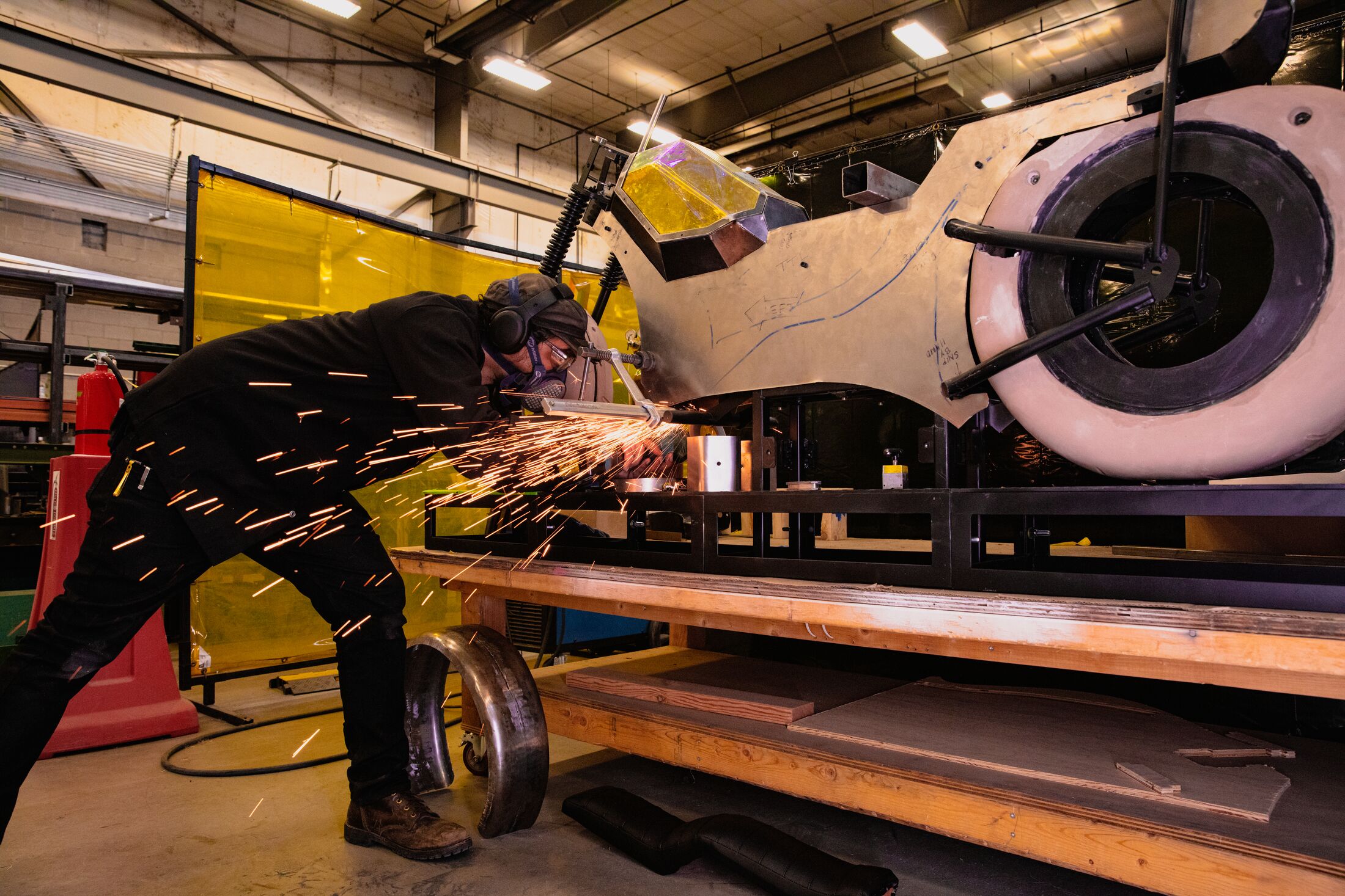 person leaning over a large metal piece and using a welder with sparks flying