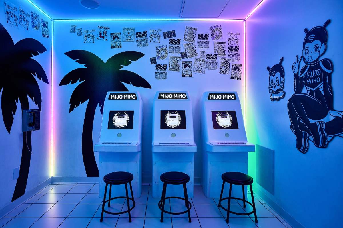 A set of 3 computer monitors sit next to each other with multicolor lighting around them and palm trees and a space character on the walls next to them.