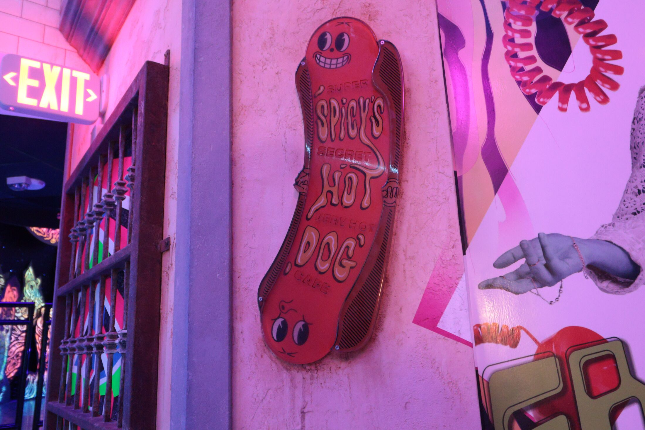 A sign shaped like a hot dog with a smiling face and the words “Spicy’s Hot Dog” on it