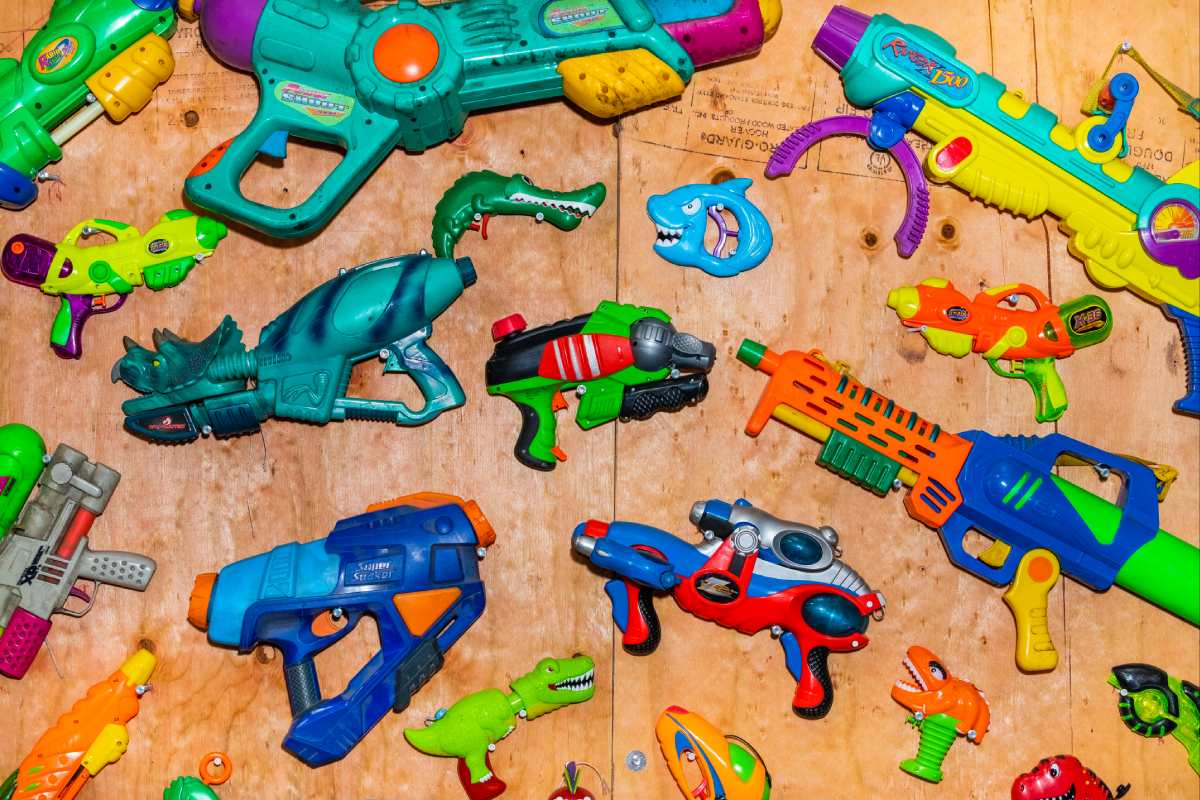 Various Super Soakers in bright colors adorn a plywood wall.